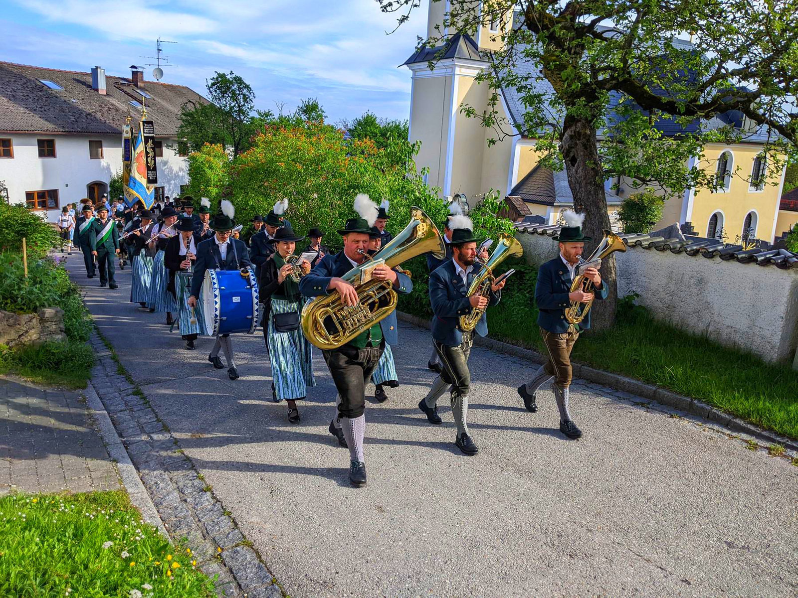 Trachtenkapelle und Trachtler ziehen an der Hittenkirchener Kirche vorbei